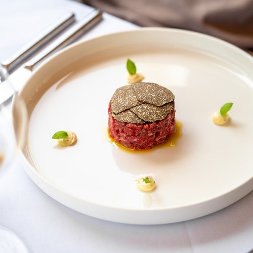 Hotel Sonnenhof Rindertatar mit Trüffelscheiben und kleinen Kräutergarnierungen auf weißem Teller