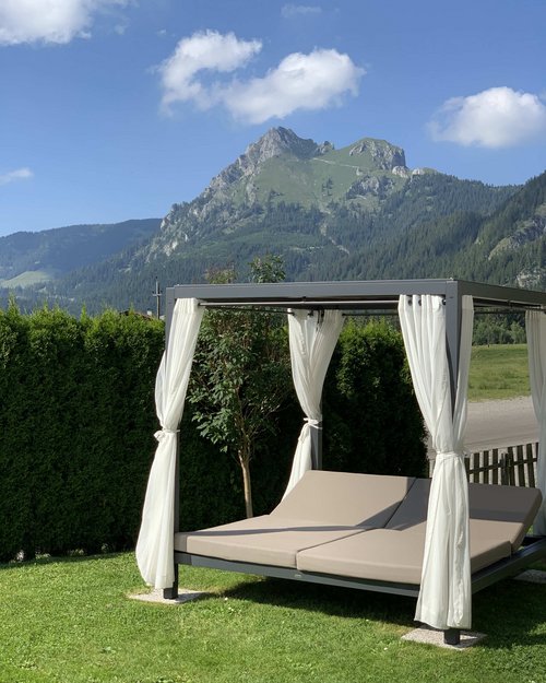 Hotel Sonnenhof Outdoor lounge bed with white curtains and mountain view on a sunny day