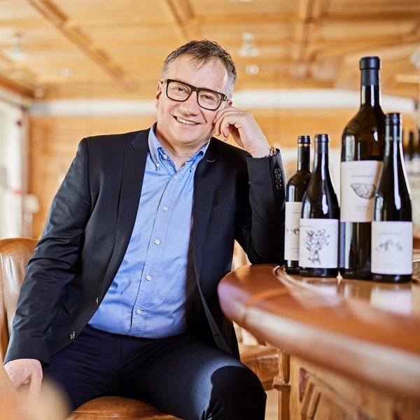 Hotel Sonnenhof Mann mit Brille in Anzug sitzt an Bar mit Weinflaschen im hellen Raum.