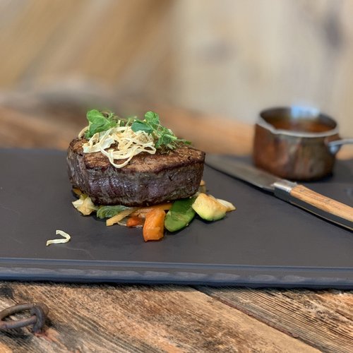 Hotel Sonnenhof Gegrilltes Steak auf Gemüse auf einer Schieferplatte mit Sauce und Messer