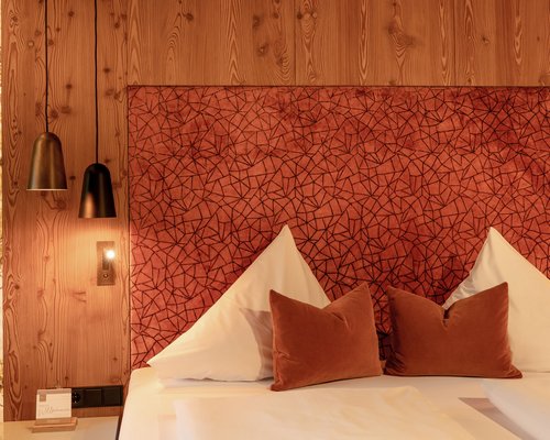 Hotel Sonnenhof Gemütliches Bett mit roten Kissen und gemustertem Kopfteil in warmem Holzinterieur