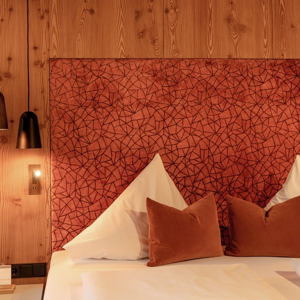 Hotel Sonnenhof Gemütliches Bett mit roten Kissen und gemustertem Kopfteil in warmem Holzinterieur