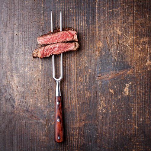 Hotel Sonnenhof Two pieces of medium rare steak on a carving fork on dark wooden table