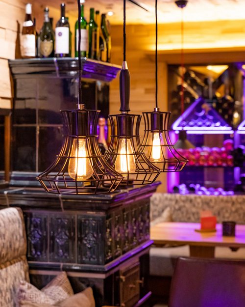 Hotel Sonnenhof Warm hanging lights above wooden table in cozy bar with bottles on shelf