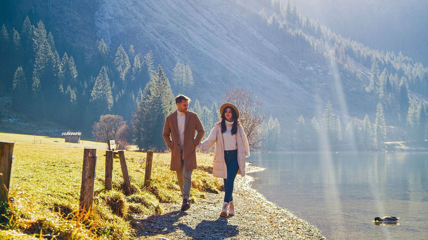 Hotel Sonnenhof Paar spaziert am Ufer eines Sees in sonniger Berglandschaft