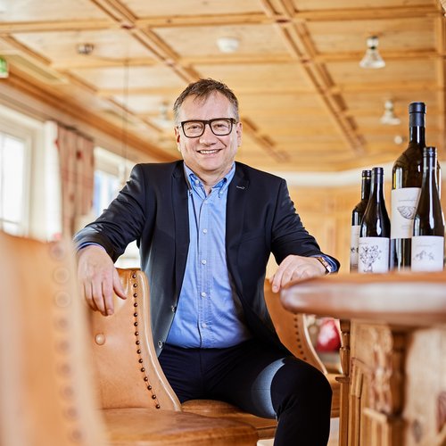 Hotel Sonnenhof Man in suit sitting at wooden table with wine bottles in rustic room