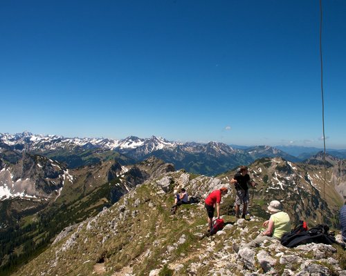 Hotel Sonnenhof Wanderer auf Gipfel mit Blick auf schneebedeckte Bergkette und blauen Himmel