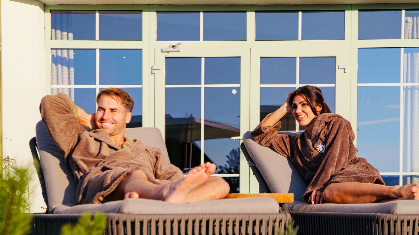 Hotel Sonnenhof Mann und Frau entspannen im Bademantel auf Liegestühlen vor einem Fenster