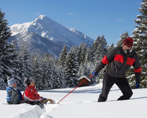 Hotel Sonnenhof Mann zieht Kinder auf Schlitten durch verschneite Winterlandschaft mit Bergen