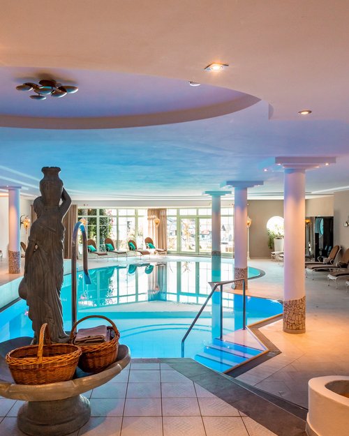 Hotel Sonnenhof Bright indoor pool area with lounge chairs and a statue holding baskets