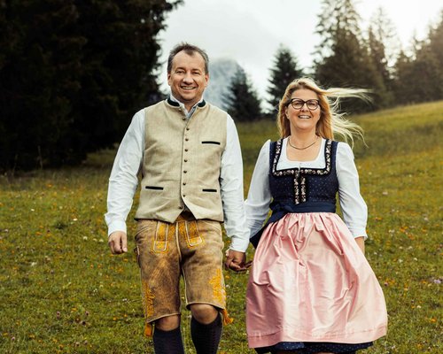 Hotel Sonnenhof Paar in traditioneller Tracht geht Hand in Hand über eine Wiese