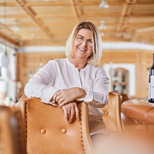 Hotel Sonnenhof Older woman with glasses smiling, sitting on leather chair in cozy room