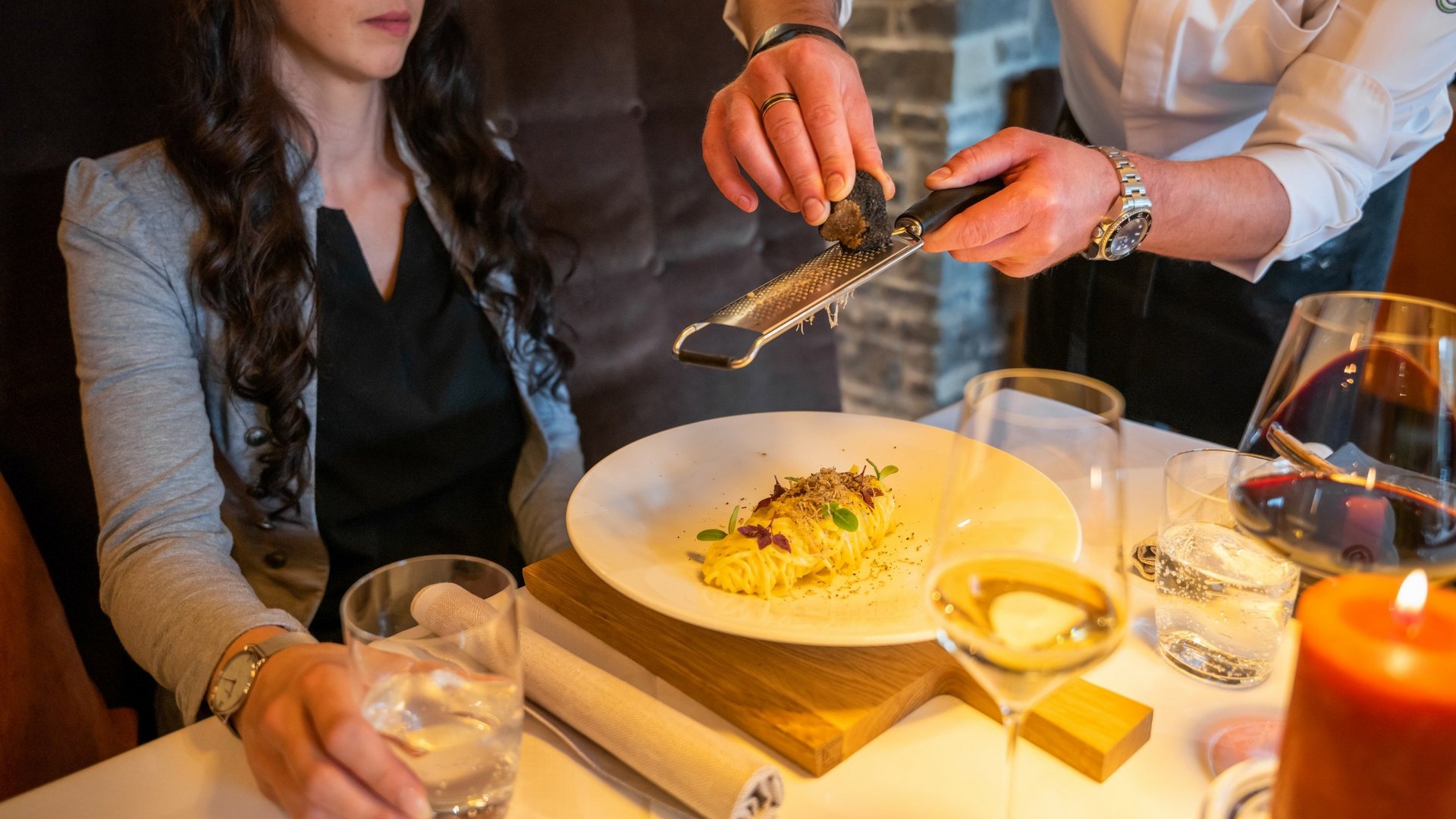 Hotel Sonnenhof Waiter grating truffle over pasta dish in an elegant restaurant