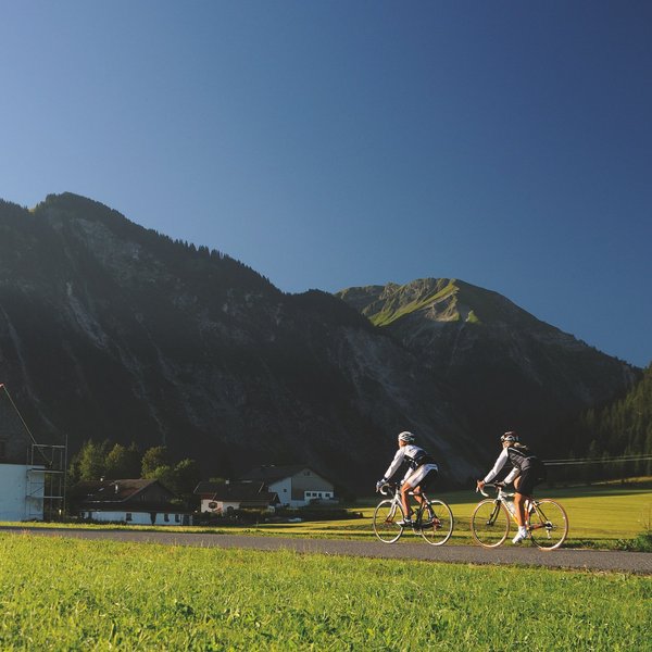 Hotel Sonnenhof Zwei Radfahrer fahren neben einer Kirche vor Bergen bei klarem Himmel