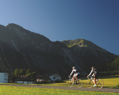 Hotel Sonnenhof Zwei Radfahrer fahren neben einer Kirche vor Bergen bei klarem Himmel