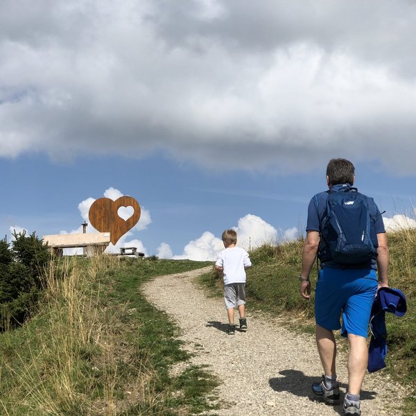 Hotel Sonnenhof Vater und Sohn wandern auf einem Weg zu einer Bank mit Herzskulptur auf einem Hügel