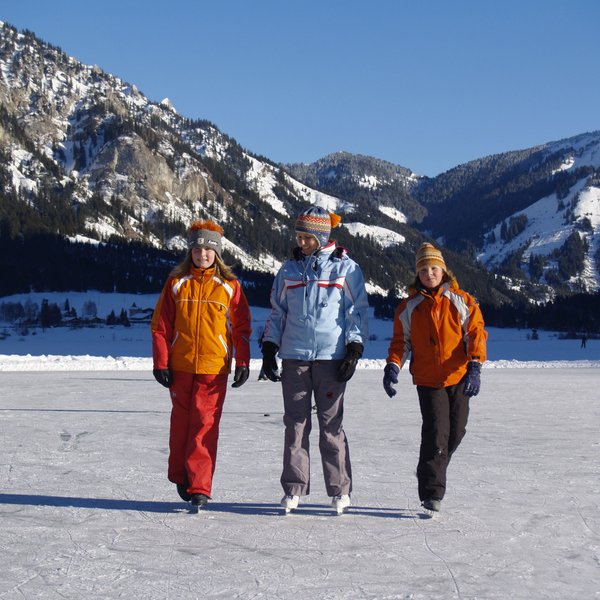Hotel Sonnenhof Drei Kinder schlittschuhlaufen auf einem gefrorenen See vor verschneiten Bergen
