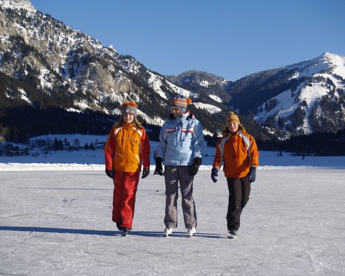 Hotel Sonnenhof Drei Kinder schlittschuhlaufen auf einem gefrorenen See vor verschneiten Bergen