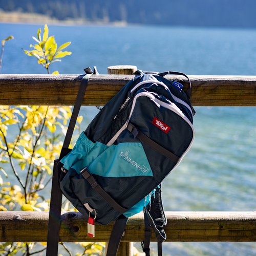 Hotel Sonnenhof Backpack hanging on wooden fence with lake and mountain background