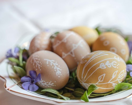 Hotel Sonnenhof Braune Ostereier mit weißen Mustern auf einem Teller mit grünen Blättern und lila Blumen