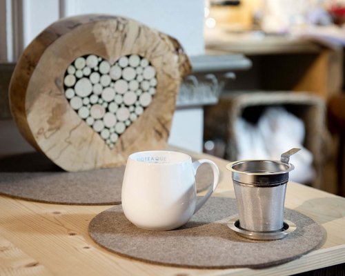 Hotel Sonnenhof Weiße Tasse und Teesieb auf einem Holztisch mit Herz-Dekoration aus Holzscheiben