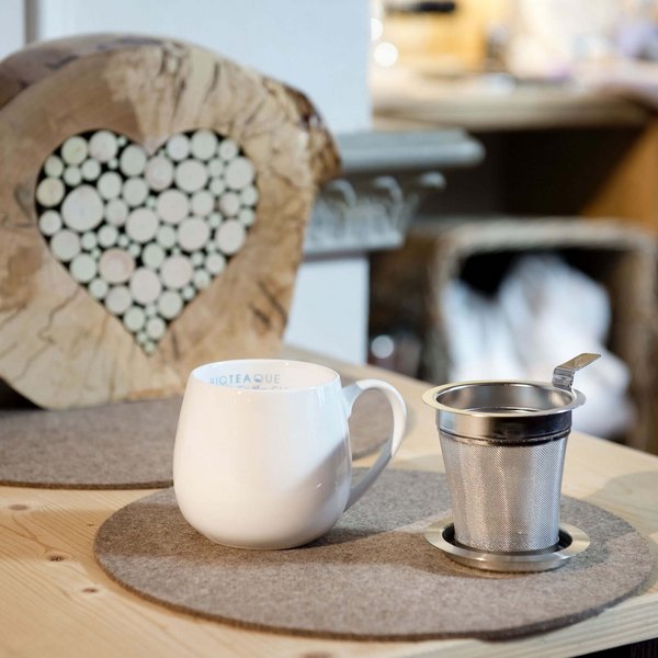 Hotel Sonnenhof Weiße Tasse und Teesieb auf einem Holztisch mit Herz-Dekoration aus Holzscheiben