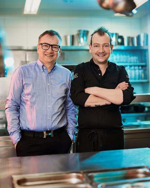 Hotel Sonnenhof Two men, a chef and a man in a shirt, standing in a restaurant kitchen