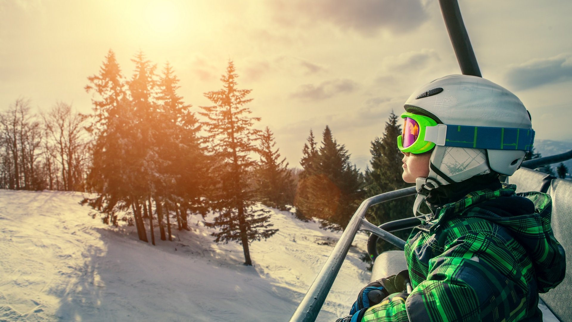 Hotel Sonnenhof Kind mit Helm und Skibrille auf Sessellift im Schnee bei Sonnenuntergang