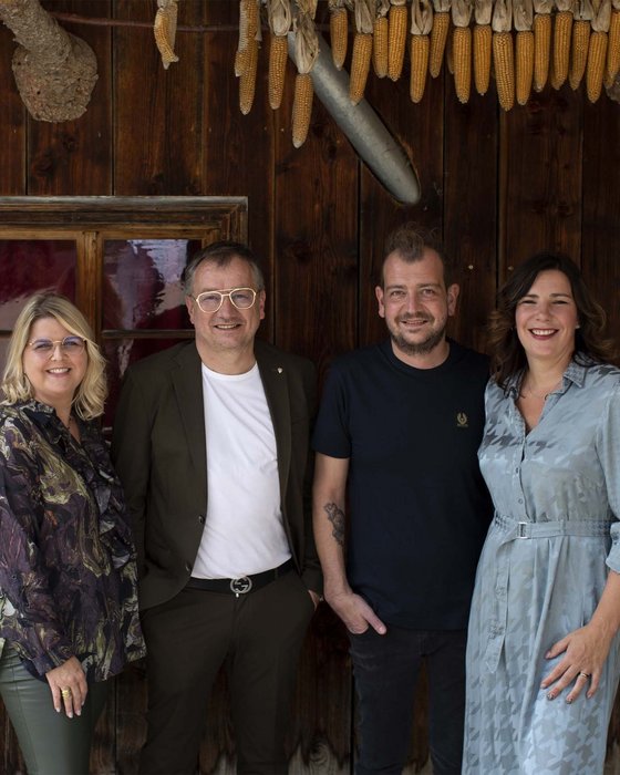 Hotel Sonnenhof Four smiling people standing in front of wooden wall with hanging corn and decorations