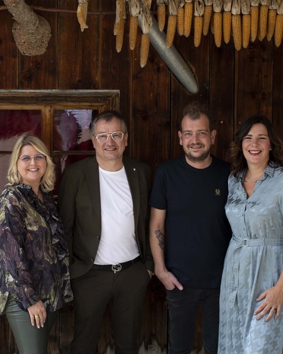 Hotel Sonnenhof Four smiling people standing in front of wooden wall with hanging corn and decorations