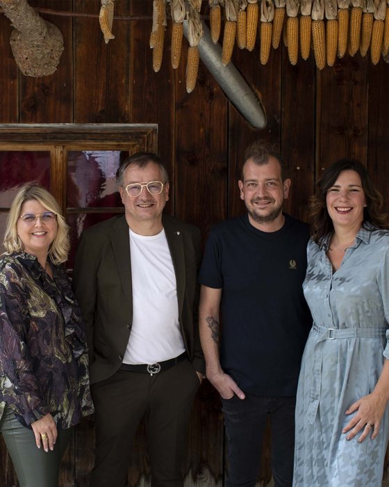 Hotel Sonnenhof Vier lächelnde Personen vor Holzwand mit hängendem Mais und Dekoration