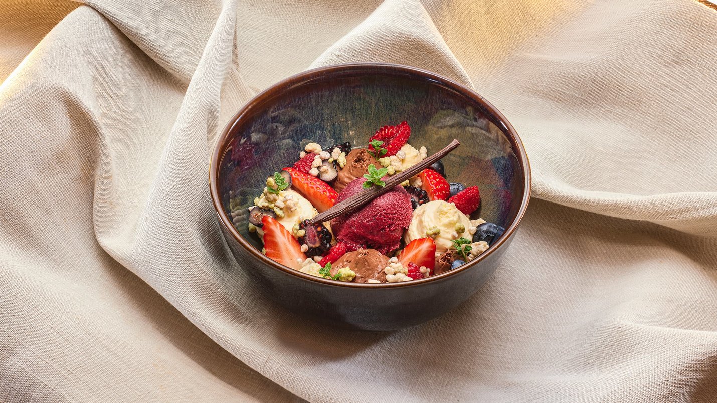 Hotel Sonnenhof Schale mit Eiscreme, Beeren, und Vanilleschote auf hellem Stoff