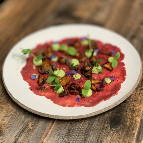 Hotel Sonnenhof Rindercarpaccio mit Pilzen, grünen Cremepunkten und Kräutern auf weißem Teller