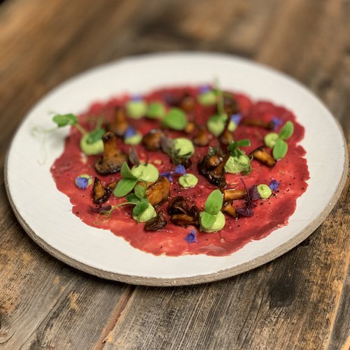 Hotel Sonnenhof Beef carpaccio with mushrooms, green cream dots, and herbs on a white plate