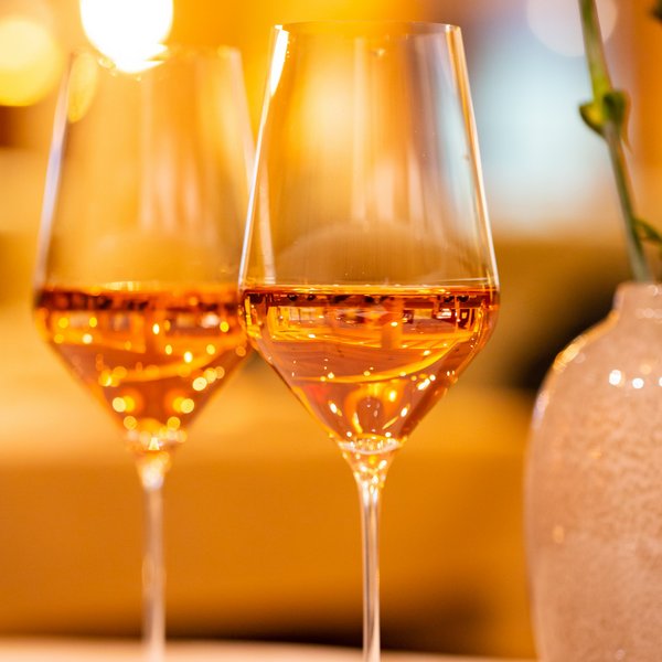 Hotel Sonnenhof Zwei Gläser mit rosé Wein neben einer Vase mit rosa Blume