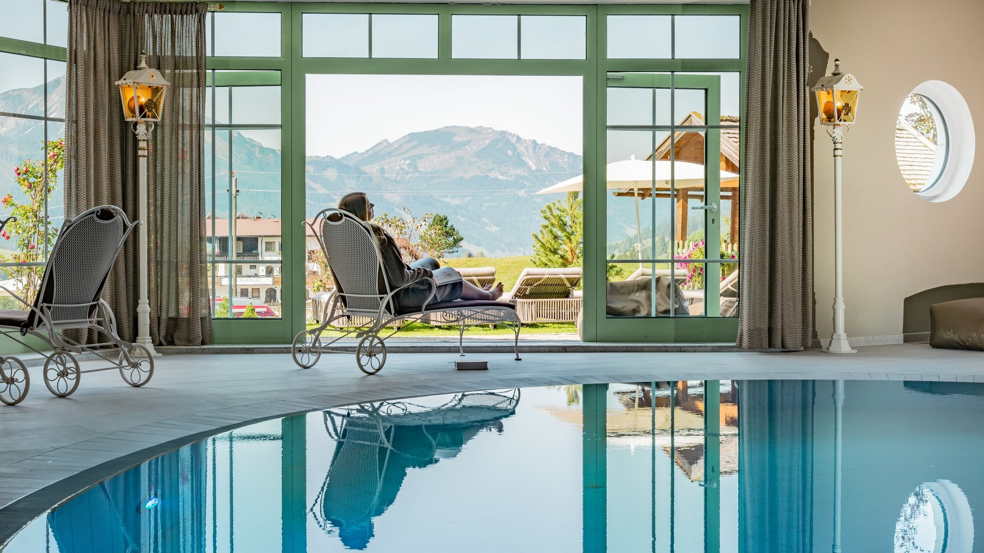 Hotel Sonnenhof Person entspannt sich auf Liege neben Indoor-Pool mit Bergblick