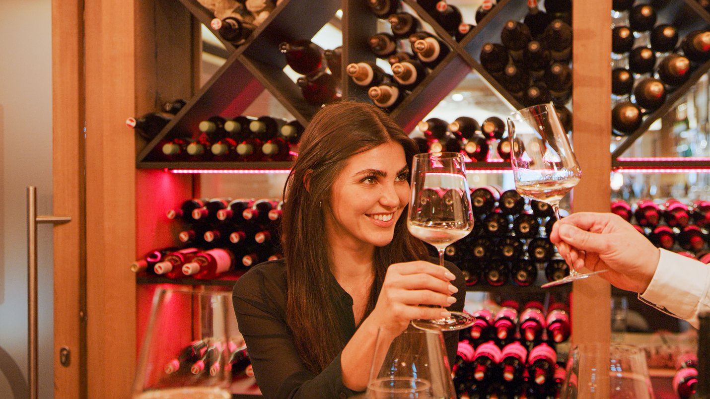 Hotel Sonnenhof Frau prostet in einem Weinkeller mit weißen Wein im Glas zu