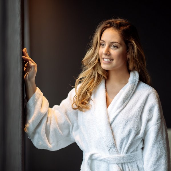 Hotel Sonnenhof Frau im weißen Bademantel blickt lächelnd aus einem Fenster