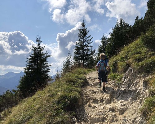 Hotel Sonnenhof Kind wandert auf felsigem Bergweg mit Kiefern und bewölktem Himmel