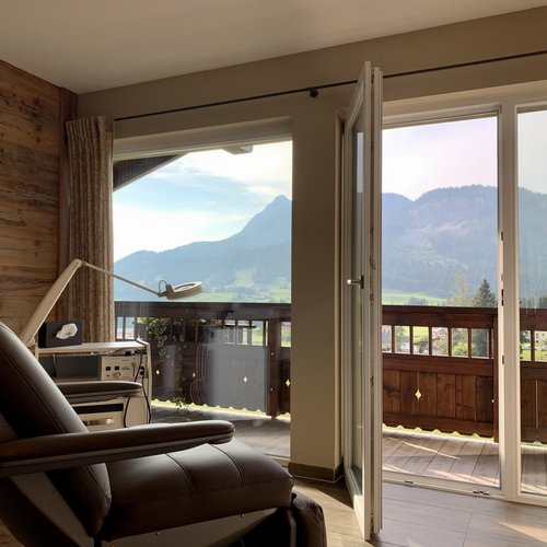 Hotel Sonnenhof Behandlungsstuhl mit Bergblick durch offene Balkonfenster in rustikalem Raum