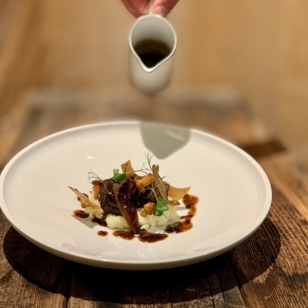 Hotel Sonnenhof Fein angerichtetes Gericht mit Fleisch und Sauce auf rustikalem Holztisch