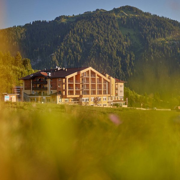 Hotel Sonnenhof umgeben von Almwiesen Berghotel mit Wiese im Vordergrund und bewaldetem Berg im Hintergrund bei Sonnenschein