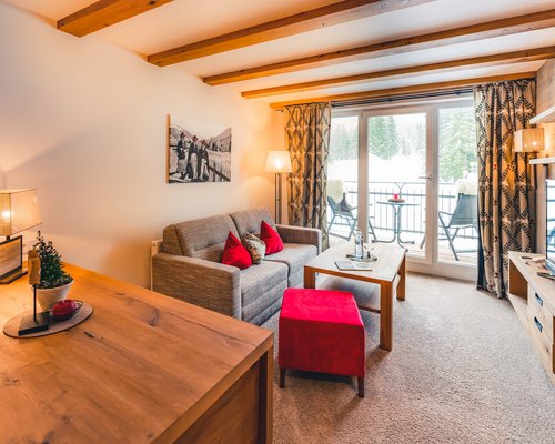 Hotel Sonnenhof Gemütliches Wohnzimmer mit Sofa, rotem Hocker und Blick auf verschneite Landschaft