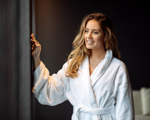 Hotel Sonnenhof Frau im weißen Bademantel, die lächelnd aus dem Fenster schaut