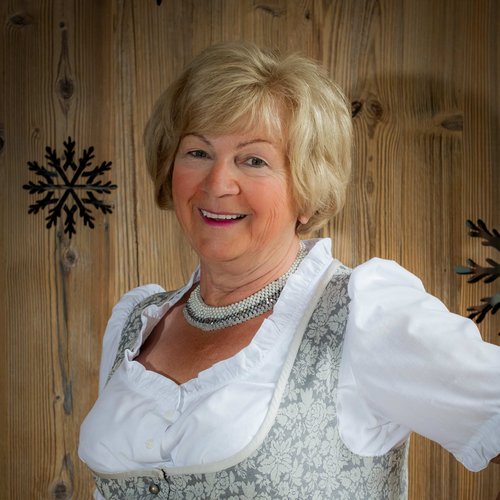 Hotel Sonnenhof Elderly woman in traditional dirndl dress standing in front of wooden wall with snowflake decor