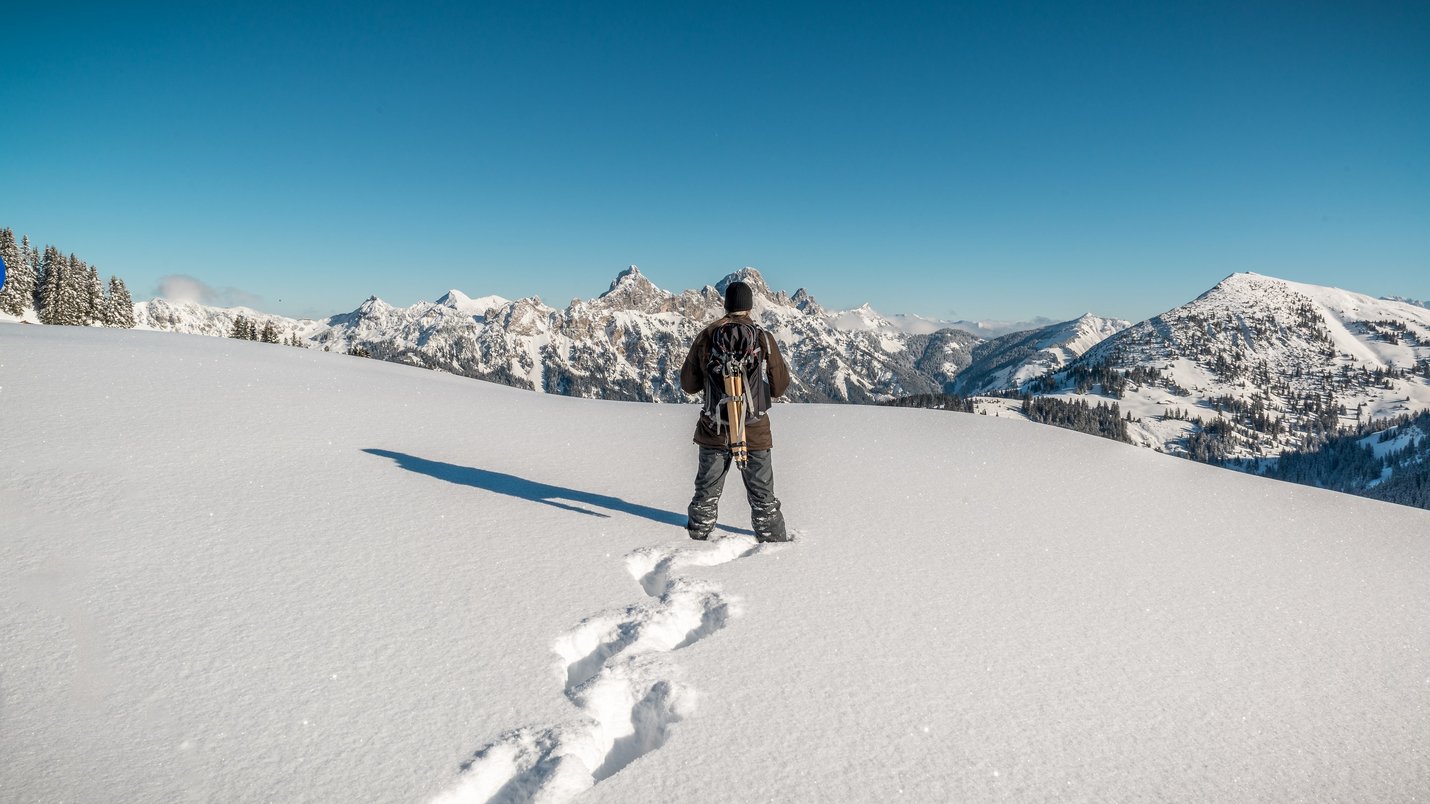 Hotel Sonnenhof Person mit Rucksack steht im tiefen Schnee vor schneebedeckten Bergen bei klarem Himmel