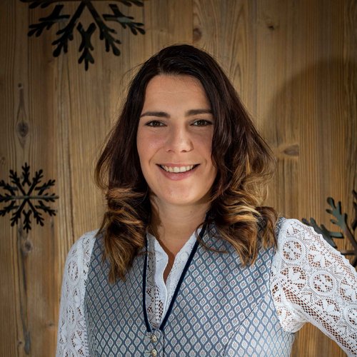 Hotel Sonnenhof Woman in traditional dress standing against a wooden wall with snowflake decor