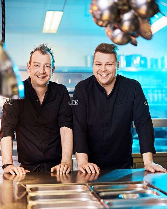 Hotel Sonnenhof Zwei lächelnde Köche in schwarzen Kochjacken in einer modernen Küchenumgebung