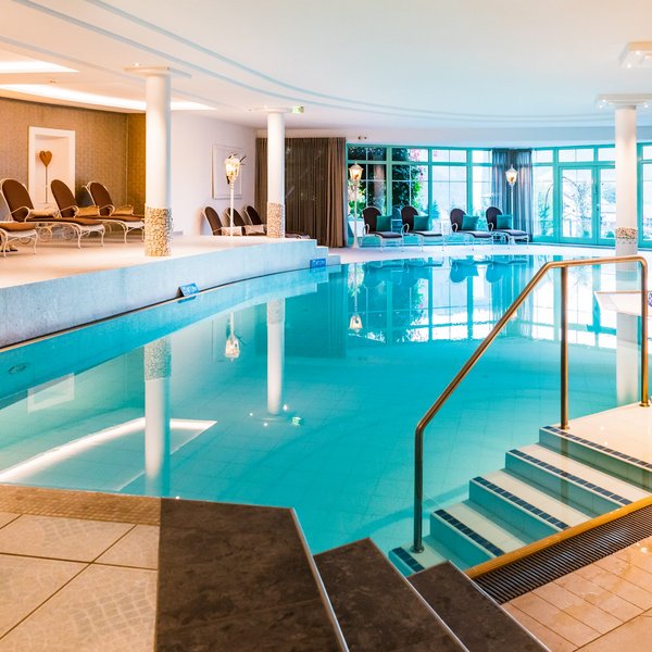 Hotel Sonnenhof Hallenbad mit Liegestühlen und großen Fenstern in einem Wellnessbereich