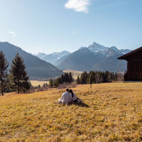 Hotel Sonnenhof Couple sitting on a meadow near a wooden cabin with mountains in the background